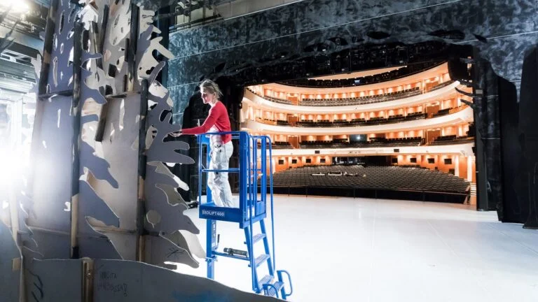 Ixolift_DACHSER_X400_People-Lifter_opera Person arbeitet auf kompakter Ixolift-Arbeitsbühne auf einer Theaterbühne vor Zuschauerrängen – sicheres Arbeiten mit ergonomischer Hebetechnik als Alternative zu Leiter