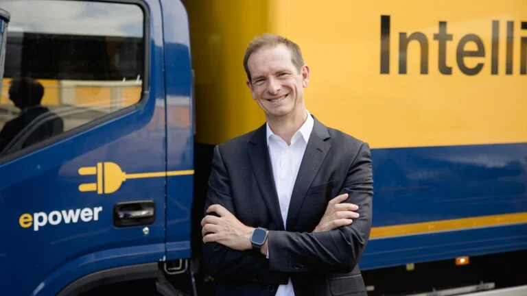 Alberto Gil Gonzalez vor einem blau-gelben Elektro-Lkw von DACHSER Iberia mit der Aufschrift „epower“ und angeschnittenem „Intelligent Logistics“-Schriftzug.